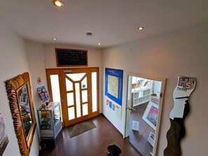 A hotel lobby with a reception desk, a glass display case, a map on the wall, and a door leading to another room.