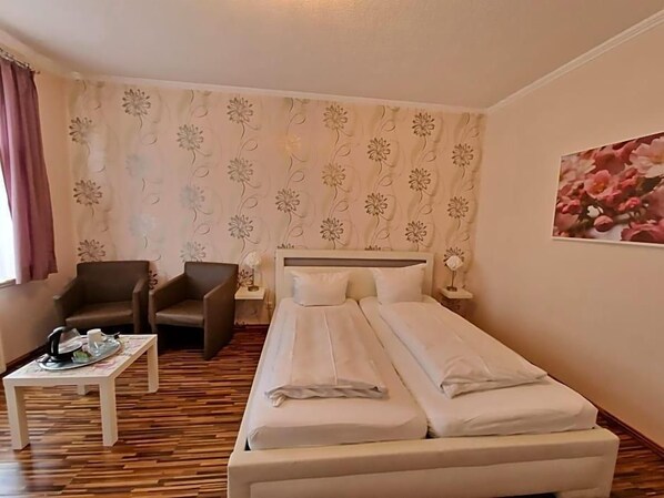 A hotel room with a bed, two chairs, a small table, and a floral-patterned curtain.