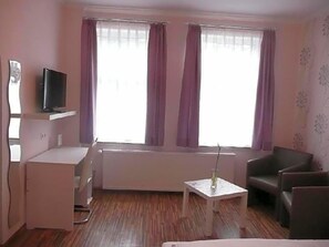 Una habitación con cama, escritorio, silla, televisor y ventana con cortinas.