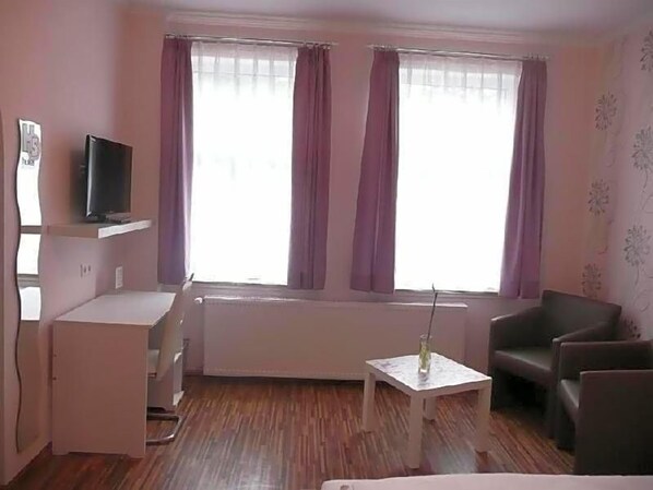 A room with a bed, a desk, a chair, a television, and a window with curtains.