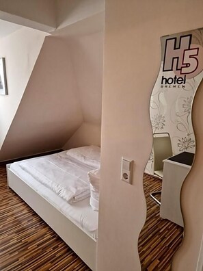 Quarto de hotel moderno com design de teto inclinado, cama com roupa de cama branca, mesa de cabeceira e uma cadeira.