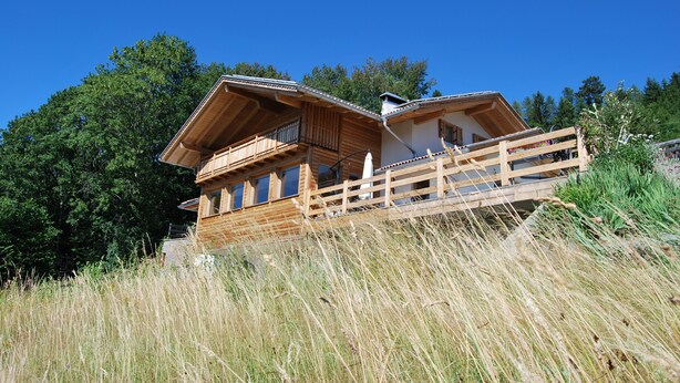 A wooden cabin with a balcony, surrounded by tall grass and trees. - The window on the dolomites (Baselga di Pinè)