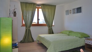 A bedroom with a bed, a window with curtains, a bedside table, and a wall with framed pictures. - The window on the dolomites (Baselga di Pinè)