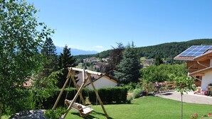 A wooden swing set in a lush garden with a view of a village and mountains in the background. - The window on the dolomites (Baselga di Pinè)