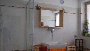 A bathroom with a glass shower enclosure, a wooden vanity with a sink, and a mirror above the vanity. - The window on the dolomites (Baselga di Pinè)