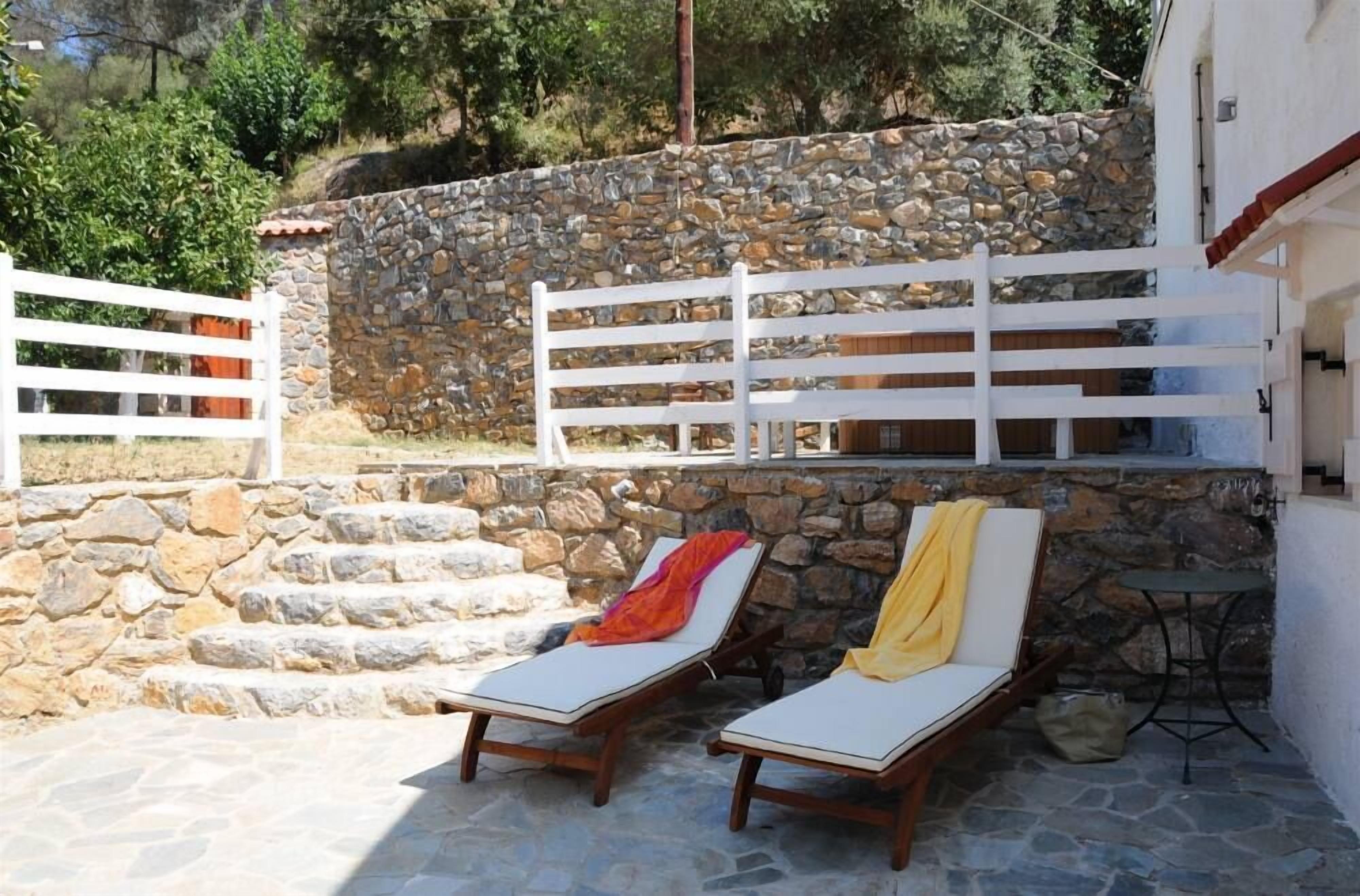 A stone wall with a white fence and two lounge chairs with cushions.