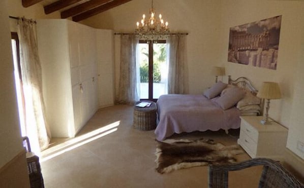 Une chambre à coucher avec un grand lit, un lustre, une fenêtre avec des rideaux, un tapis et un tableau au mur.