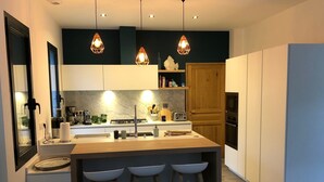 A modern kitchen with a central island, bar stools, pendant lighting, and a variety of appliances.