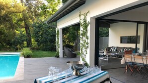 An outdoor patio with a pool, a table set with glasses and a bowl, and a seating area with a sofa and chairs.