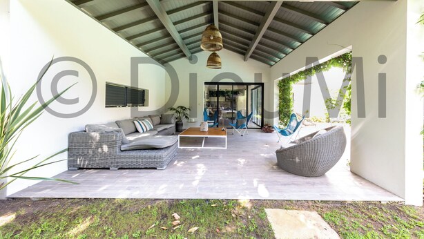 A spacious outdoor living area with a modern design, featuring a sofa set, a dining table, and a large wicker chair.