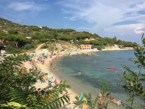 Una playa con agua cristalina, sombrillas y gente.
