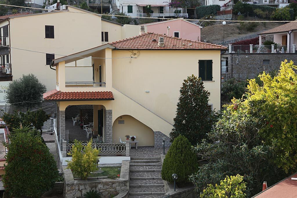 A two-story building with a red-tiled roof, a balcony, and a stone staircase leading to the entrance.