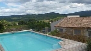 A rectangular swimming pool with a wooden deck surrounding it, set against a backdrop of mountains and a cloudy sky. - Villa w/Lg Private Pool In Beautiful Languedoc-Roussillon Countryside-WiFi (Durban-Corbières)