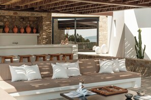 A modern outdoor seating area with a stone wall, a sofa with cushions, and a wooden table with a book and a board game.