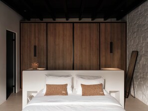 A modern bedroom with a large bed, wooden wardrobe, and a stone wall.