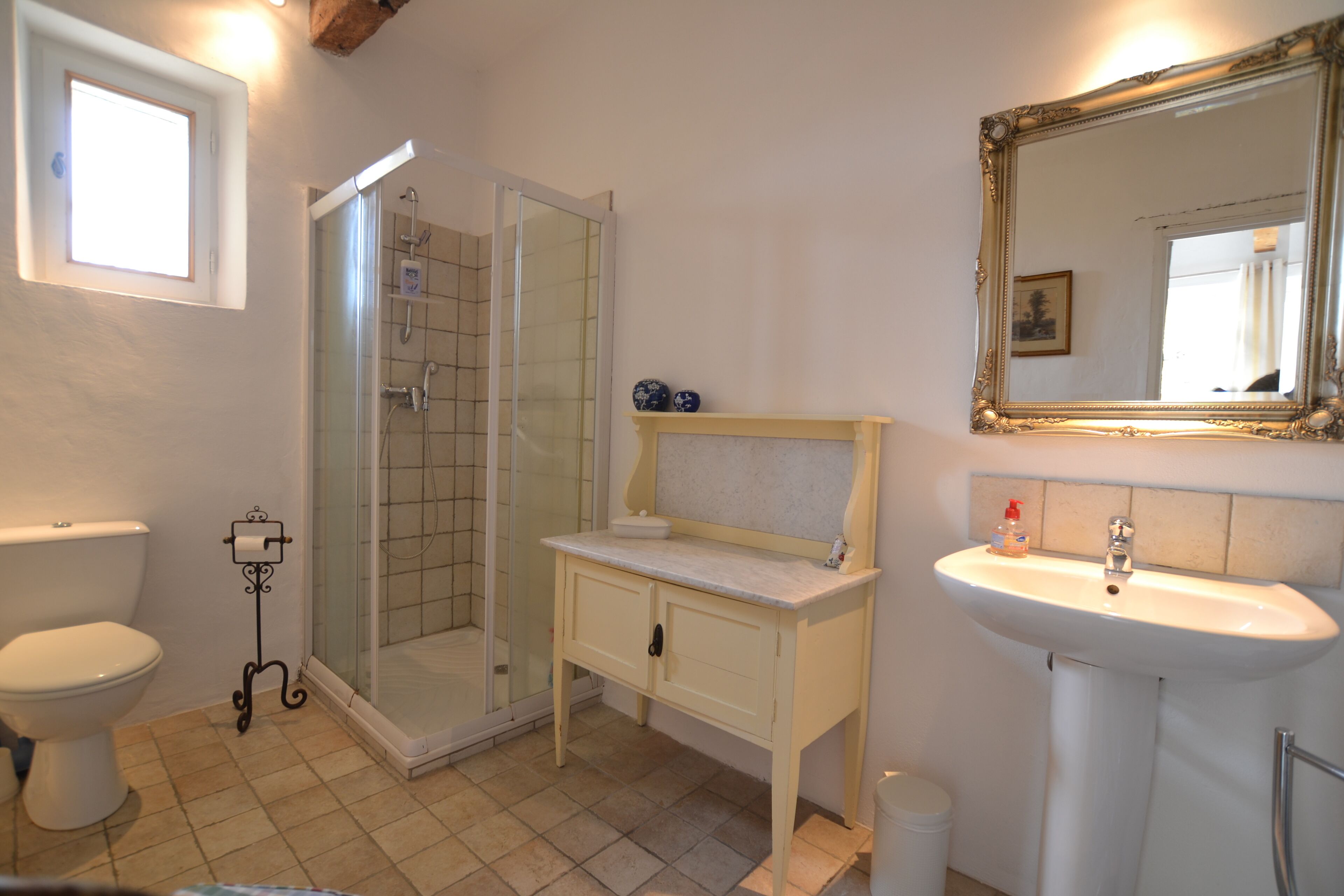 Une salle de bain comprenant des toilettes, un lavabo, une douche avec une porte en verre et un meuble-lavabo avec un miroir.