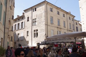 Uma rua movimentada com uma banca de mercado e edifícios históricos ao fundo.