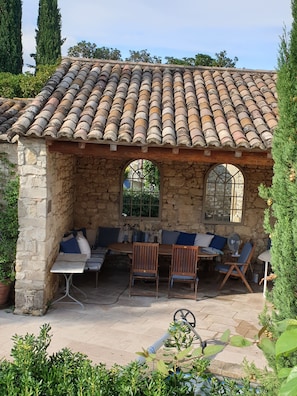 A stone building with a tiled roof, stone walls, and a seating area with a table and chairs. - Mas de la Chapelle ~ Stone Maison de Maitre with a Heated Private Pool         (Garrigues-Sainte-Eulalie)