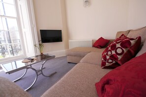Ein Wohnzimmer mit einer Couch, einem Glastisch, einem Flachbildfernseher und einer Heizung.