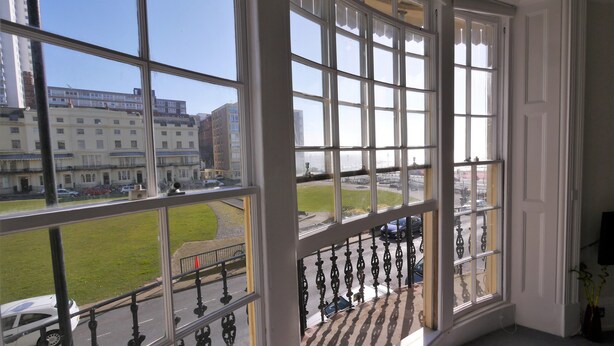 A room with large windows offering a view of the street and buildings outside. - Regency Retreat  - Stylish Apartment with sea views and balcony. Great Location. (Brighton)