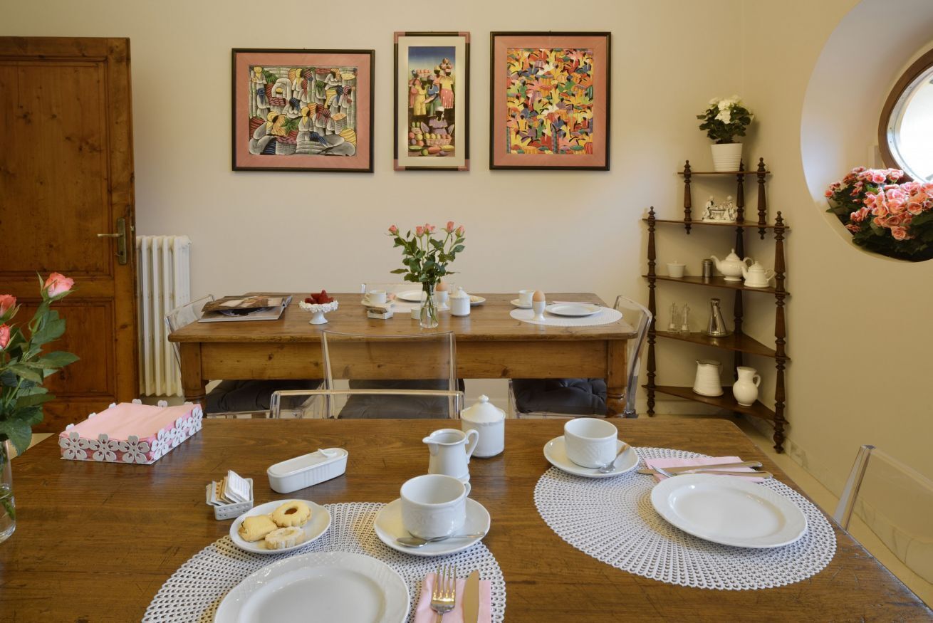 A dining area with a wooden table set for four, surrounded by chairs. There are three framed artworks on the wall above the table.