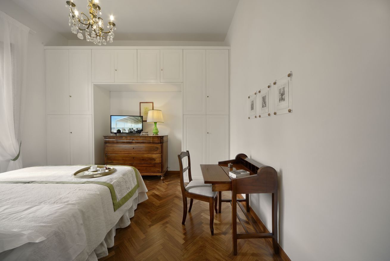 Ein Schlafzimmer mit einem Bett, einer Holzkommode, einem Fernseher, einem Tisch mit Stühlen und einer Chandelier.
