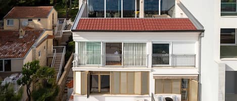 A two-story residential building with a red-tiled roof, balconies with railings, and a satellite dish.