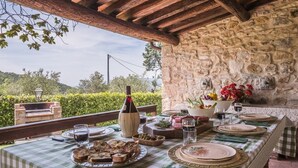 Un espace de restauration en plein air avec des murs en pierre, une table dressée avec des assiettes, des verres et une bouteille de vin.