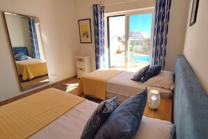 A hotel room with two beds, a small dresser, a mirror, and a view of the pool area.