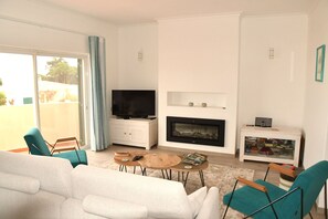 A modern living room with a sofa, two chairs, a coffee table, a TV, a fireplace, and a bookshelf.