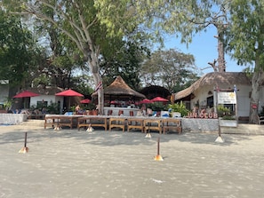 An outdoor seating area with wooden tables and red umbrellas, a thatched-roof structure, and a sign for 'Jintana Herb Sauna'.