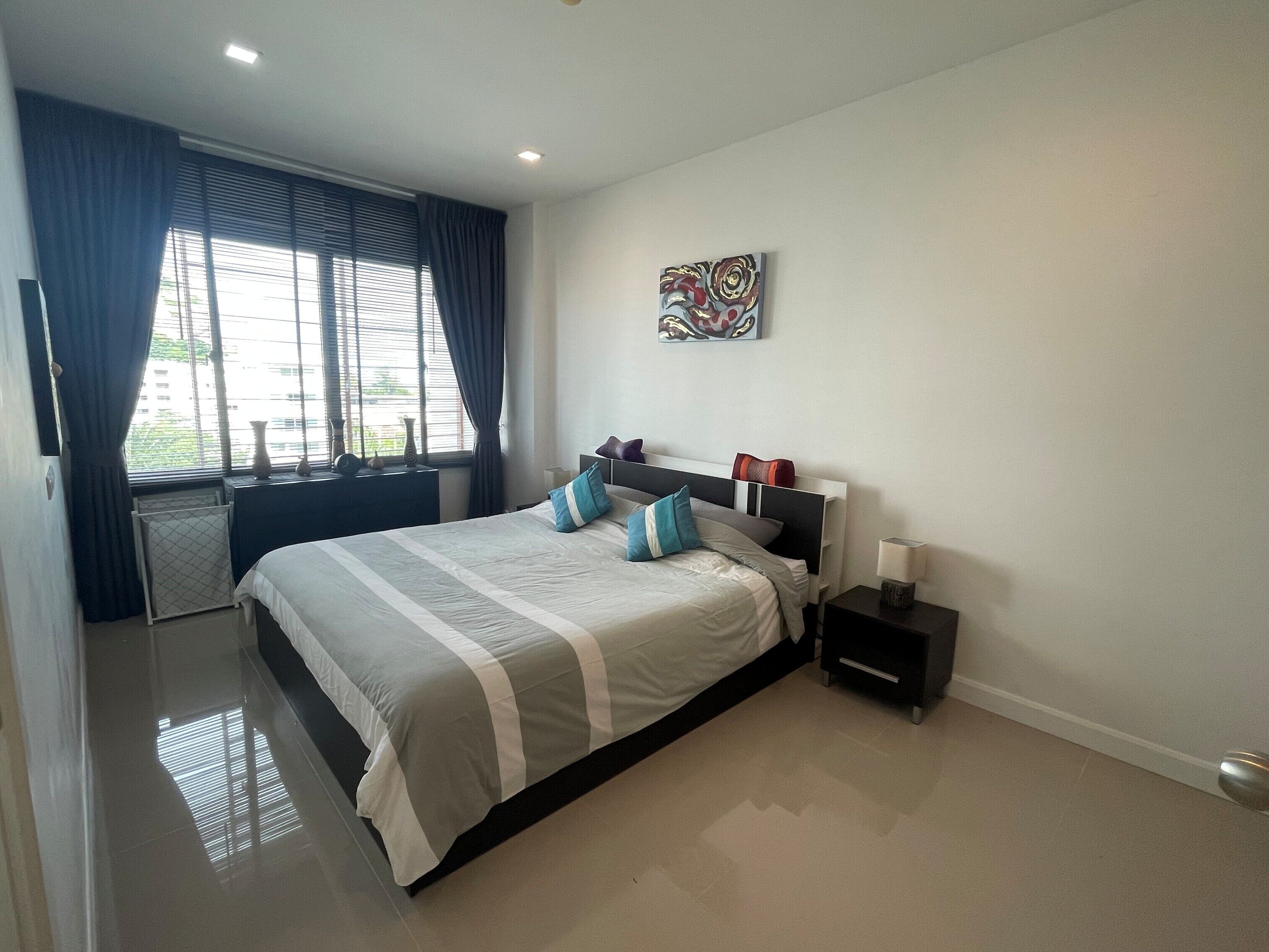 Une chambre moderne avec un grand lit, une table de chevet, une fenêtre avec des rideaux et une œuvre d’art accrochée au mur.