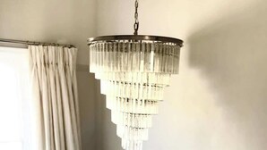 Una escalera con barandilla blanca, un candelabro y un ventanal con cortinas.