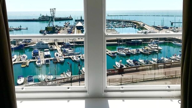 Un puerto deportivo con barcos amarrados, una grúa y un puente al fondo.
