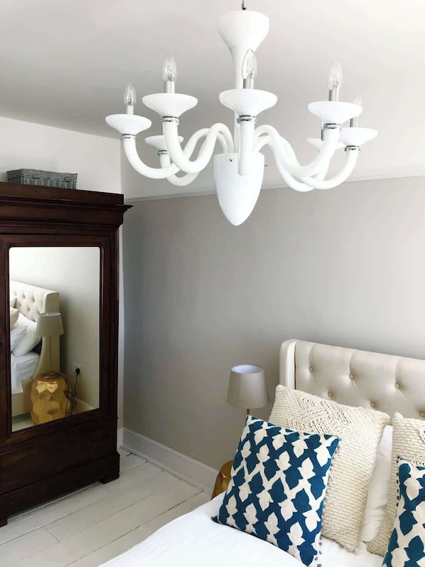 A bedroom with a large bed, a wooden dresser, a mirror, and a white chandelier.