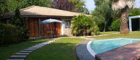 Ein Garten mit Swimmingpool, einem Kiesweg und einer Holzterrasse mit Gartenmöbeln.