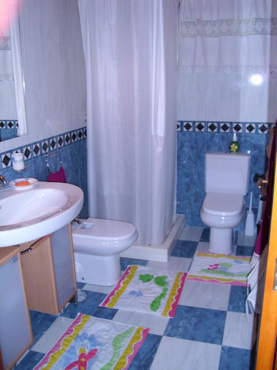 A bathroom with a sink, toilet, and shower curtain. The floor has a checkered pattern with colorful mats.