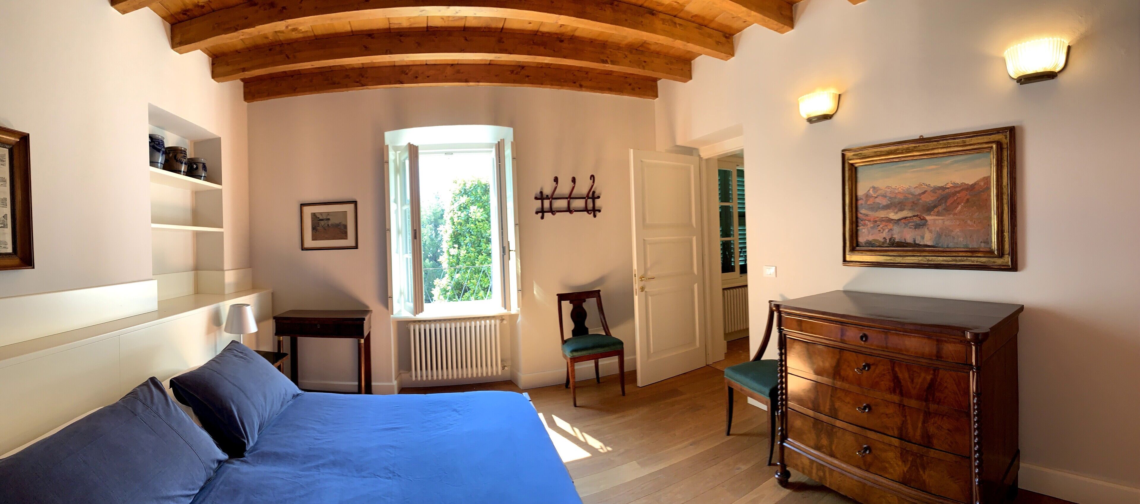 A bedroom with a bed, a dresser, a chair, a radiator, a window, and a painting on the wall.