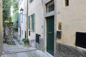 A narrow cobblestone street with buildings on either side, a green door, and a stone wall on the left.
