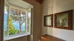 Ein Zimmer mit großem Fenster mit Blick auf einen Baum und ein Gewässer. An der Wand hängen zwei gerahmte Bilder.