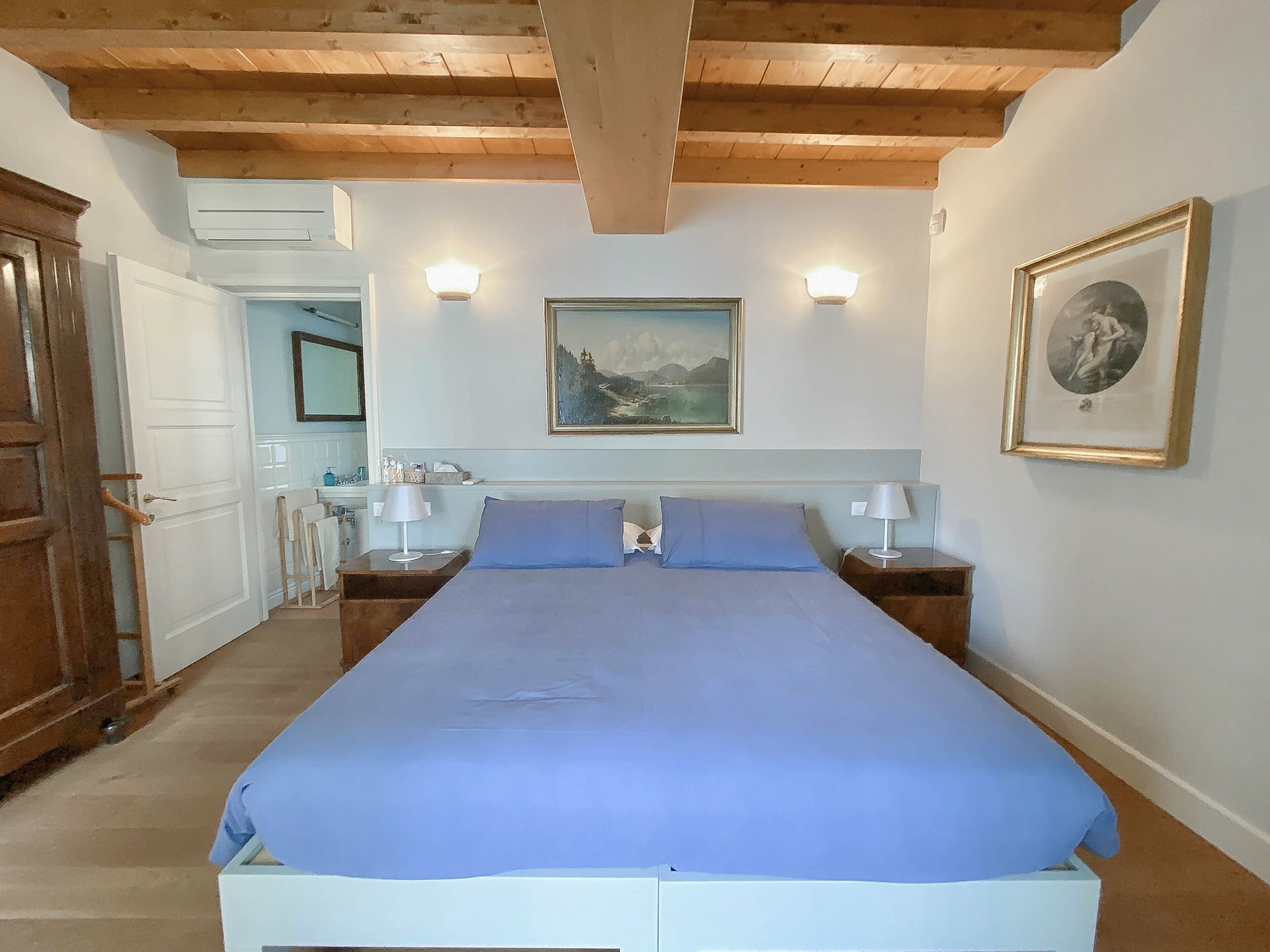Une chambre à coucher avec un grand lit, deux tables de chevet avec des lampes, un tableau au mur et un plafond en bois.