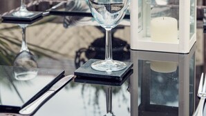 A table with two wine glasses, a candle in a lantern, and cutlery on a glass table.