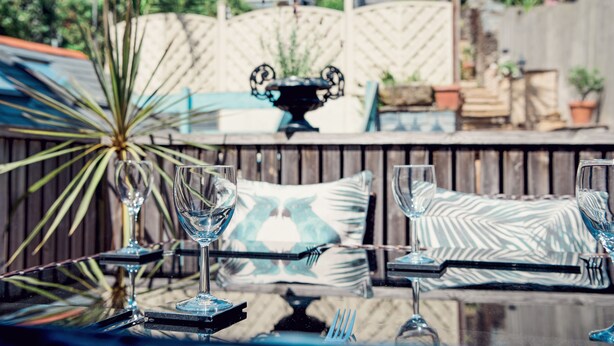 A patio with a table set for dining, featuring a glass-top table, metal chairs, and a decorative plant.