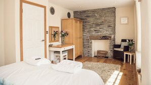 A bedroom with a bed, a desk, a wardrobe, a stone fireplace, and a wicker basket.