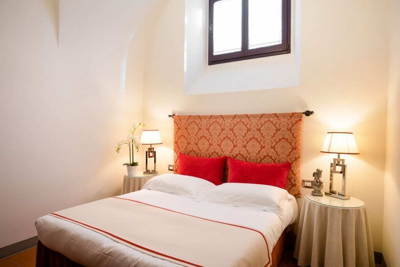 Un lit bien fait, avec une literie blanche et rouge, deux tables de chevet avec des lampes et une fenêtre au-dessus du lit.