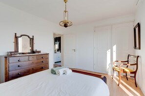 Quarto com cómoda de madeira, uma cama, uma cadeira e um guarda-roupa.