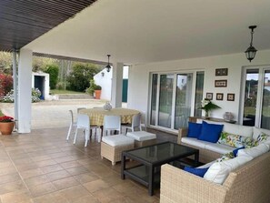 En overdækket terrasse med et bord, stole, en sofa og et sofabord i glas.
