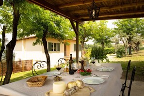 Ein Essbereich im Freien mit Tisch, der für eine Mahlzeit gedeckt ist, umgeben von Bäumen und einem Gebäude im Hintergrund.
