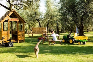 Une cabane en bois servant de maison de jeu, avec un banc et un petit tracteur jouet, dans un parc.