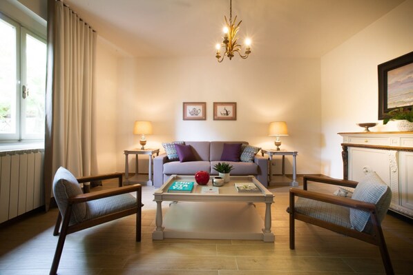 Ein Wohnzimmer mit einer Couch, zwei Sesseln, einem Couchtisch, einer Deckenleuchte und zwei Lampen.